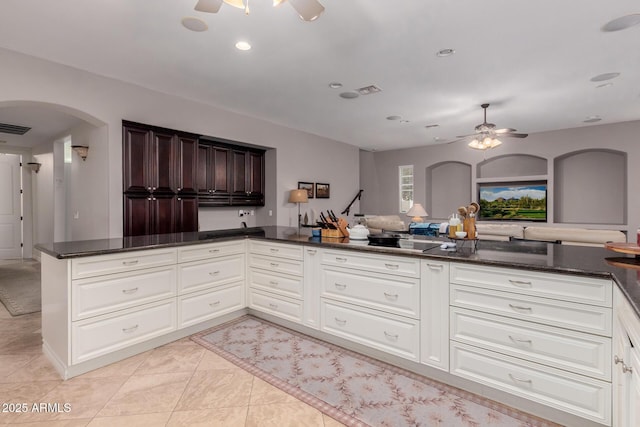 kitchen with ceiling fan, visible vents, arched walkways, and dark stone countertops