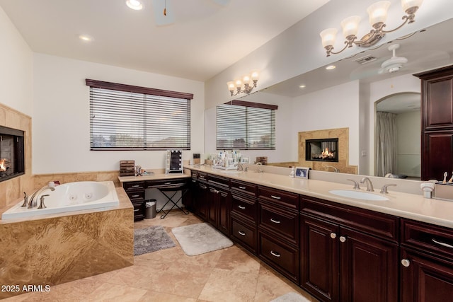 full bath with visible vents, a premium fireplace, a ceiling fan, a sink, and a jetted tub