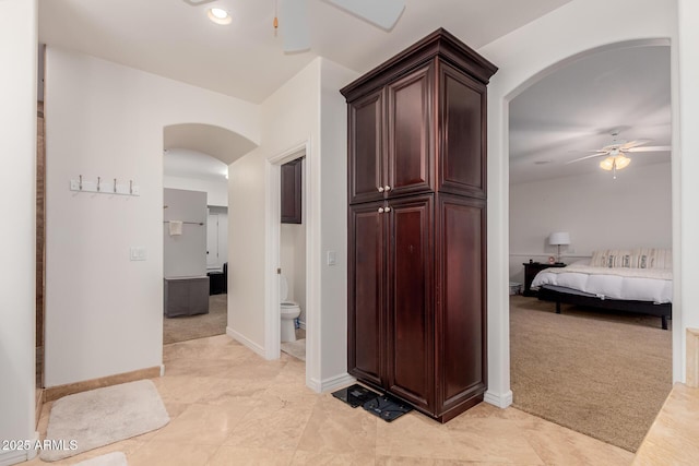 hallway featuring arched walkways, light carpet, and baseboards