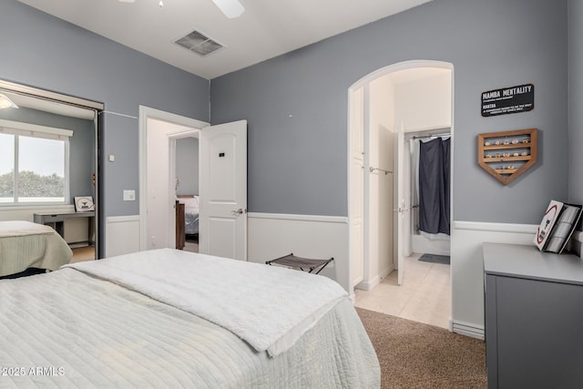 bedroom with arched walkways, light tile patterned floors, light colored carpet, a ceiling fan, and visible vents