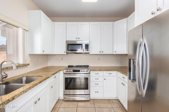 kitchen with light stone countertops, stainless steel appliances, sink, white cabinetry, and light tile patterned flooring