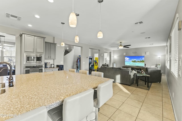 kitchen with a kitchen breakfast bar, appliances with stainless steel finishes, gray cabinetry, ceiling fan, and pendant lighting