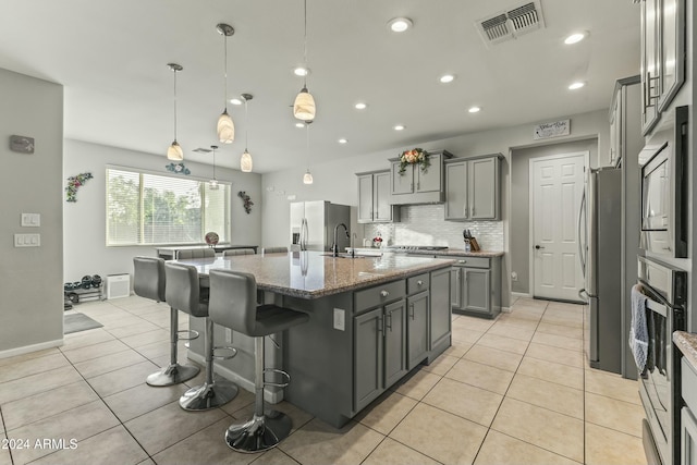 14575 W Orange Dr, Litchfield Park, AZ 85340 - kitchen with gray cabinetry, stainless steel appliances, backsplash, dark stone countertops, and a kitchen island with sink