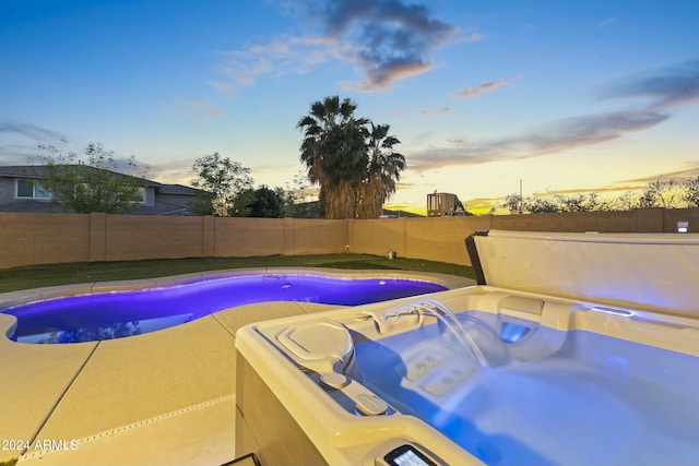 pool at dusk featuring a hot tub