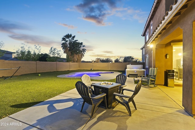 patio terrace at dusk featuring a pool with hot tub, a yard, and an outdoor fire pit