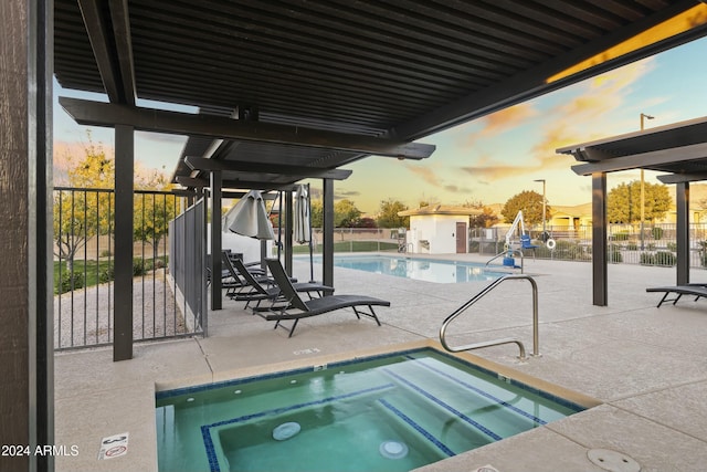 pool at dusk with a patio area and a community hot tub