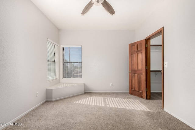 unfurnished bedroom with a walk in closet, a closet, light colored carpet, and ceiling fan