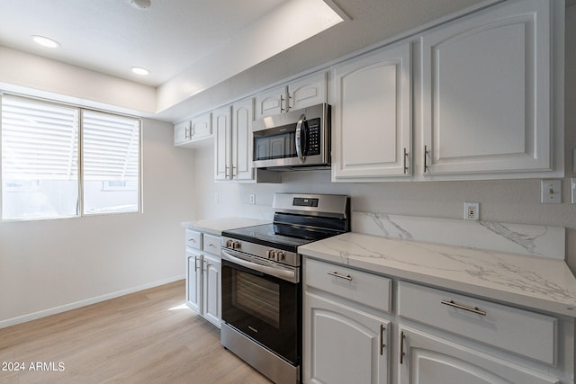 kitchen with appliances with stainless steel finishes, light hardwood / wood-style floors, white cabinetry, and light stone countertops