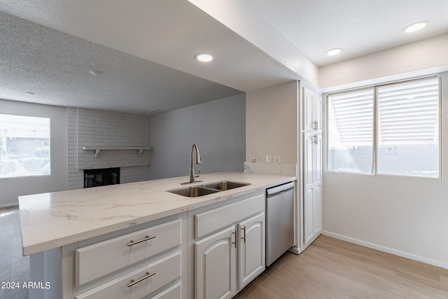 kitchen with sink, white cabinetry, kitchen peninsula, a brick fireplace, and stainless steel dishwasher