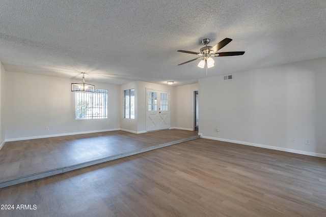 empty room with ceiling fan with notable chandelier, a textured ceiling, and hardwood / wood-style floors