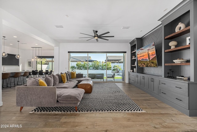 living room featuring light wood-type flooring, built in features, and ceiling fan