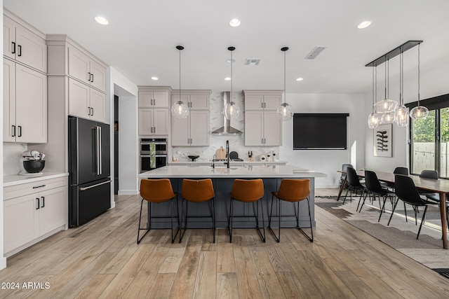 kitchen featuring pendant lighting, an island with sink, stainless steel appliances, and wall chimney range hood