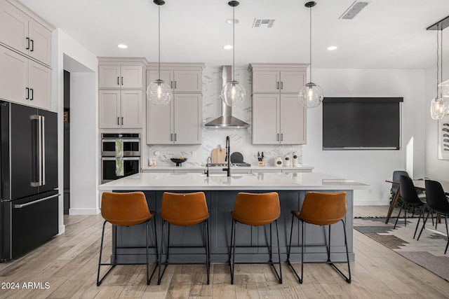 kitchen with a center island with sink, decorative light fixtures, wall chimney range hood, and stainless steel appliances