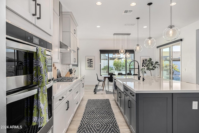 kitchen featuring pendant lighting, a center island with sink, gray cabinetry, and sink