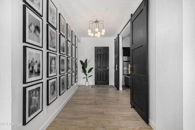 hall with a barn door, a chandelier, and light wood-type flooring