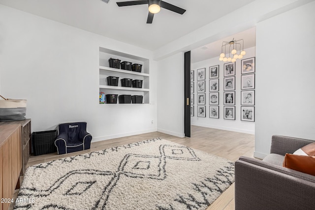 sitting room with built in shelves, light hardwood / wood-style floors, and ceiling fan with notable chandelier