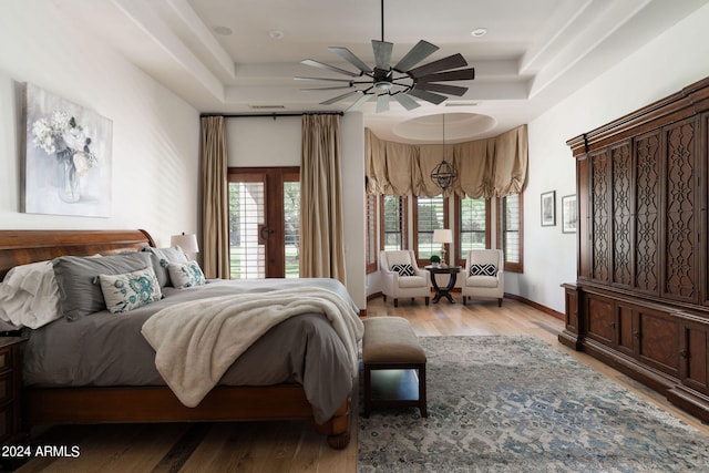 bedroom featuring a raised ceiling, light wood-type flooring, and ceiling fan