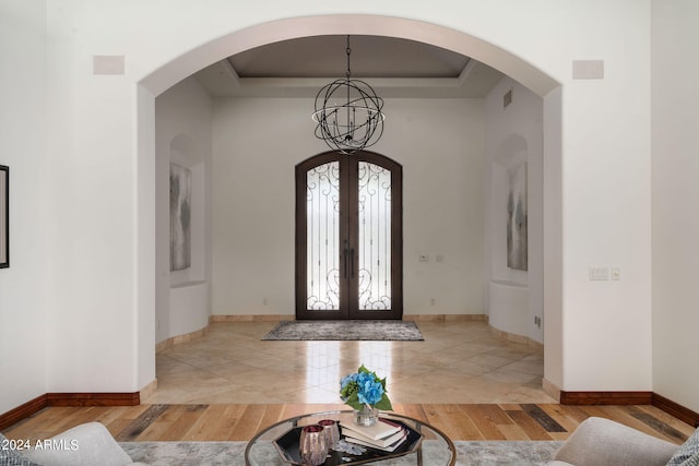 foyer entrance with a chandelier, light hardwood / wood-style flooring, a tray ceiling, and french doors