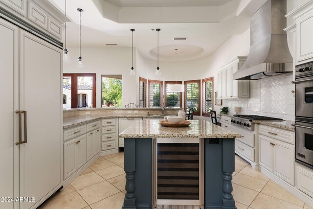 kitchen featuring wall chimney exhaust hood, kitchen peninsula, wine cooler, a center island, and pendant lighting