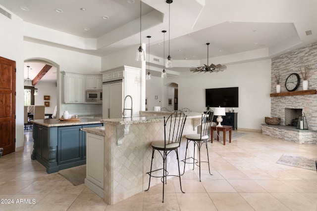 kitchen with hanging light fixtures, a tray ceiling, a kitchen bar, built in appliances, and a fireplace