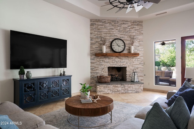 tiled living room featuring ceiling fan, a tray ceiling, and a fireplace