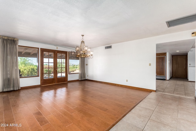 unfurnished room featuring a textured ceiling, light hardwood / wood-style flooring, french doors, and a notable chandelier