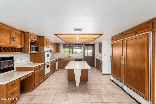 kitchen featuring pendant lighting, a center island, built in appliances, sink, and light tile patterned floors