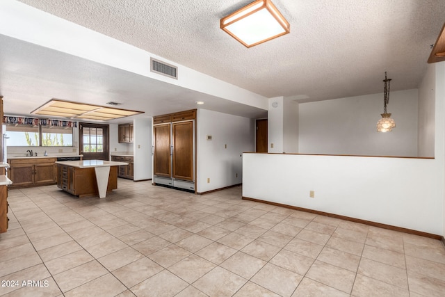 kitchen with a textured ceiling, decorative light fixtures, light tile patterned floors, and a center island