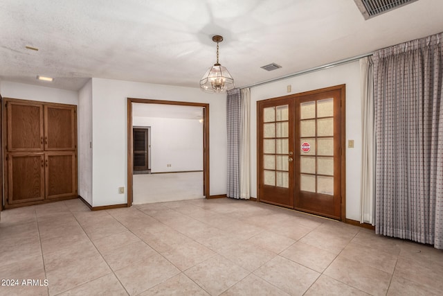 spare room with a textured ceiling, an inviting chandelier, light tile patterned floors, and french doors