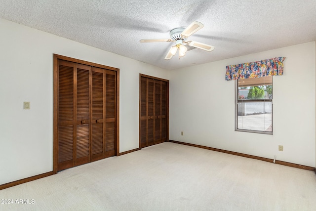 unfurnished bedroom with ceiling fan, multiple closets, a textured ceiling, and carpet floors