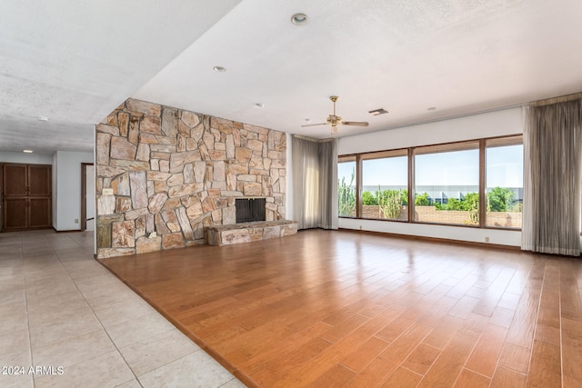 unfurnished living room with ceiling fan, a stone fireplace, a textured ceiling, and light hardwood / wood-style flooring