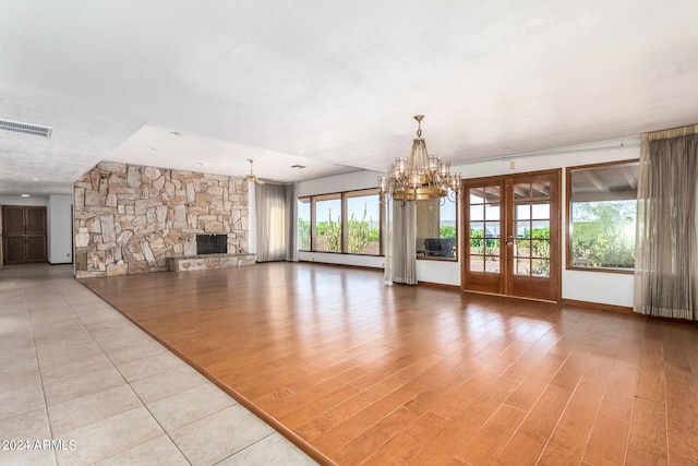 unfurnished living room with french doors, a stone fireplace, a textured ceiling, a notable chandelier, and light hardwood / wood-style floors