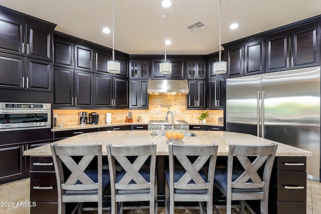 35443 N 87th Pl, Scottsdale, AZ 85266 - kitchen with under cabinet range hood, appliances with stainless steel finishes, a kitchen island with sink, a kitchen breakfast bar, and recessed lighting