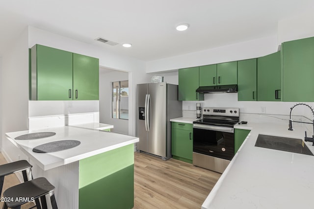 kitchen with appliances with stainless steel finishes, sink, light wood-type flooring, green cabinetry, and a breakfast bar