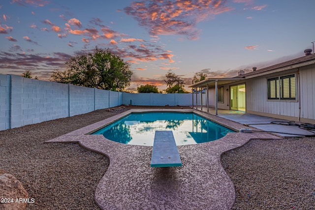 pool at dusk with a patio area and a diving board