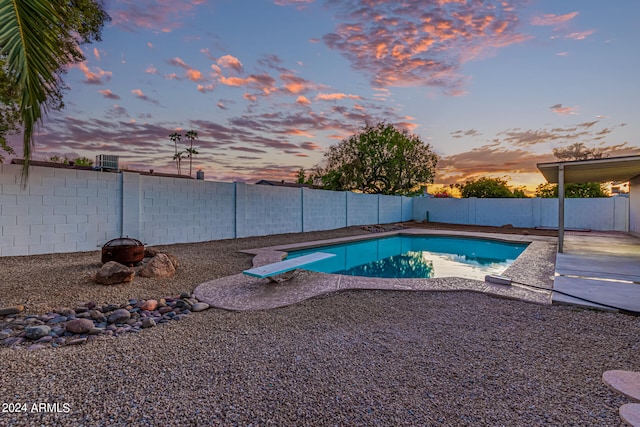 pool at dusk featuring a patio and a diving board