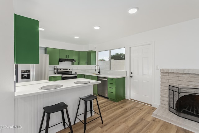 kitchen featuring light hardwood / wood-style flooring, stainless steel appliances, a breakfast bar, and green cabinetry