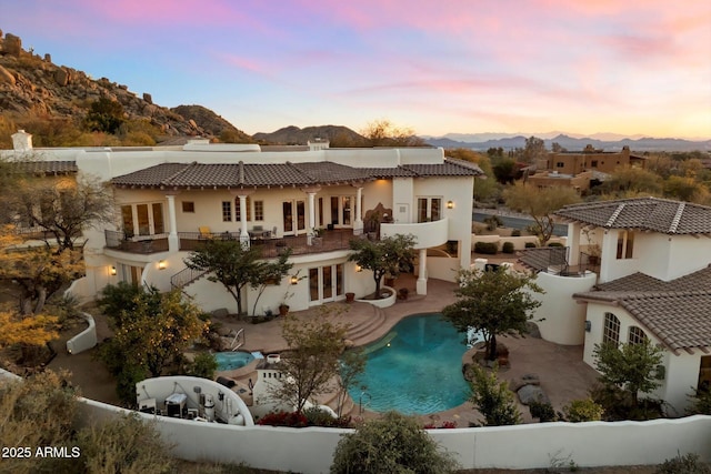 back house at dusk with a patio area, a mountain view, french doors, and a balcony