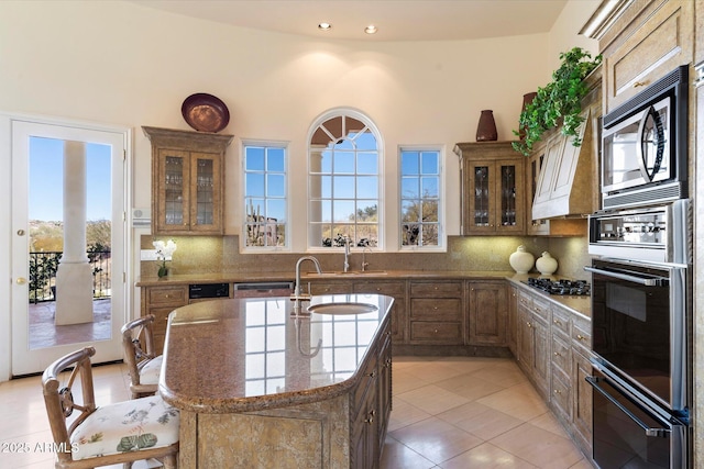 kitchen with stainless steel appliances, tasteful backsplash, sink, light tile patterned flooring, and a center island with sink