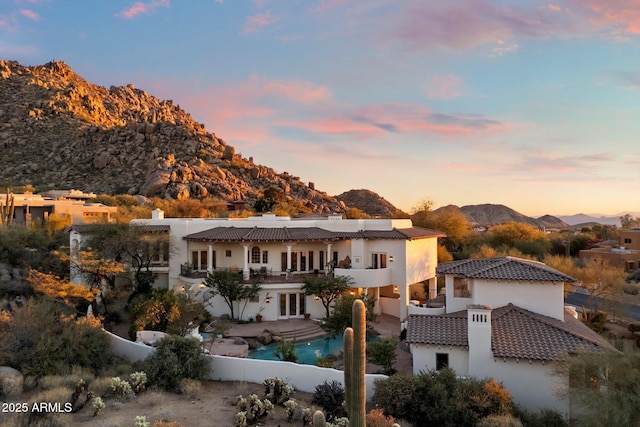 back house at dusk with a mountain view, a patio area, and a balcony