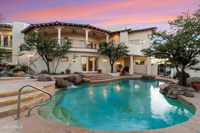 pool at dusk with ceiling fan, pool water feature, a patio area, and french doors