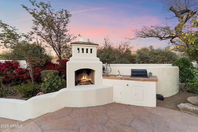 patio terrace at dusk featuring an outdoor fireplace and an outdoor kitchen