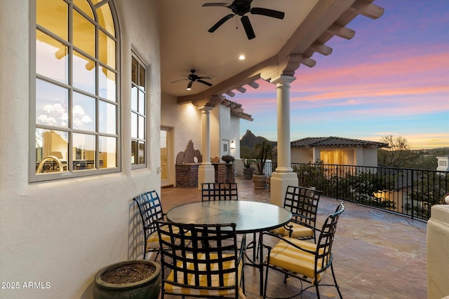 patio terrace at dusk featuring ceiling fan and exterior kitchen