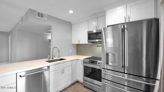 kitchen featuring white cabinets, sink, light hardwood / wood-style flooring, decorative backsplash, and stainless steel appliances