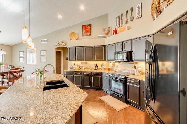 kitchen with pendant lighting, sink, light stone counters, black appliances, and light hardwood / wood-style flooring