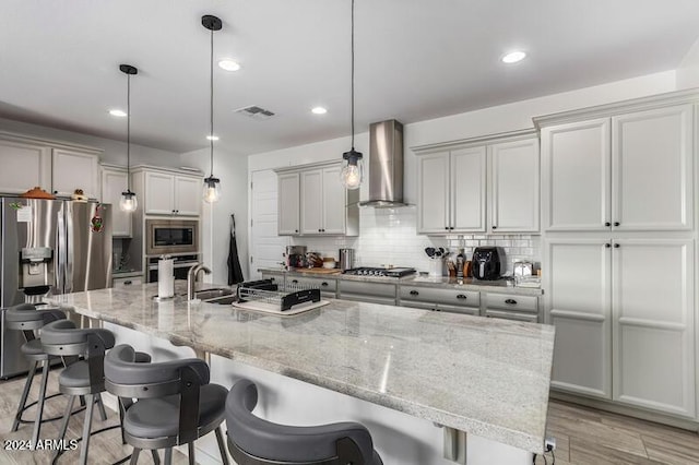 kitchen featuring decorative light fixtures, stainless steel appliances, wall chimney range hood, and a large island