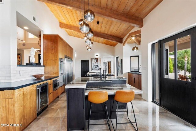 kitchen featuring beam ceiling, an island with sink, high vaulted ceiling, beverage cooler, and wooden ceiling