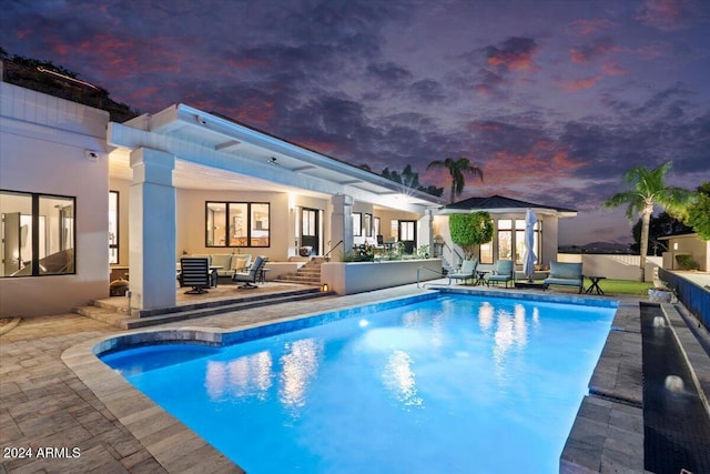 pool at dusk featuring outdoor lounge area and a patio