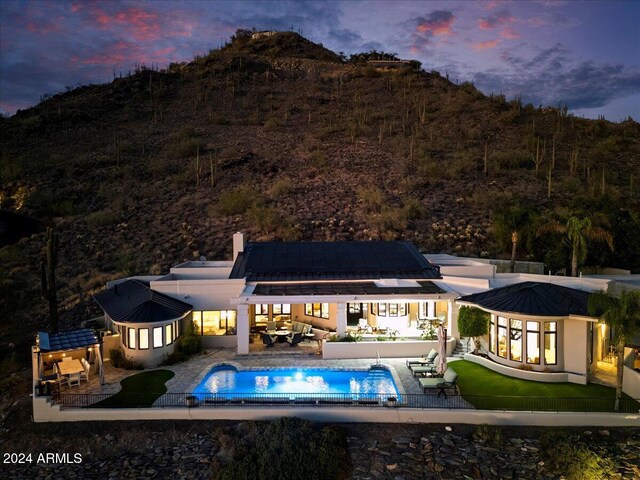 back house at dusk with a patio area, an outdoor living space, and solar panels