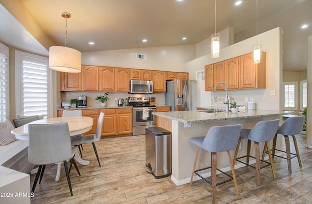 kitchen featuring visible vents, light stone counters, light wood-style flooring, appliances with stainless steel finishes, and a peninsula